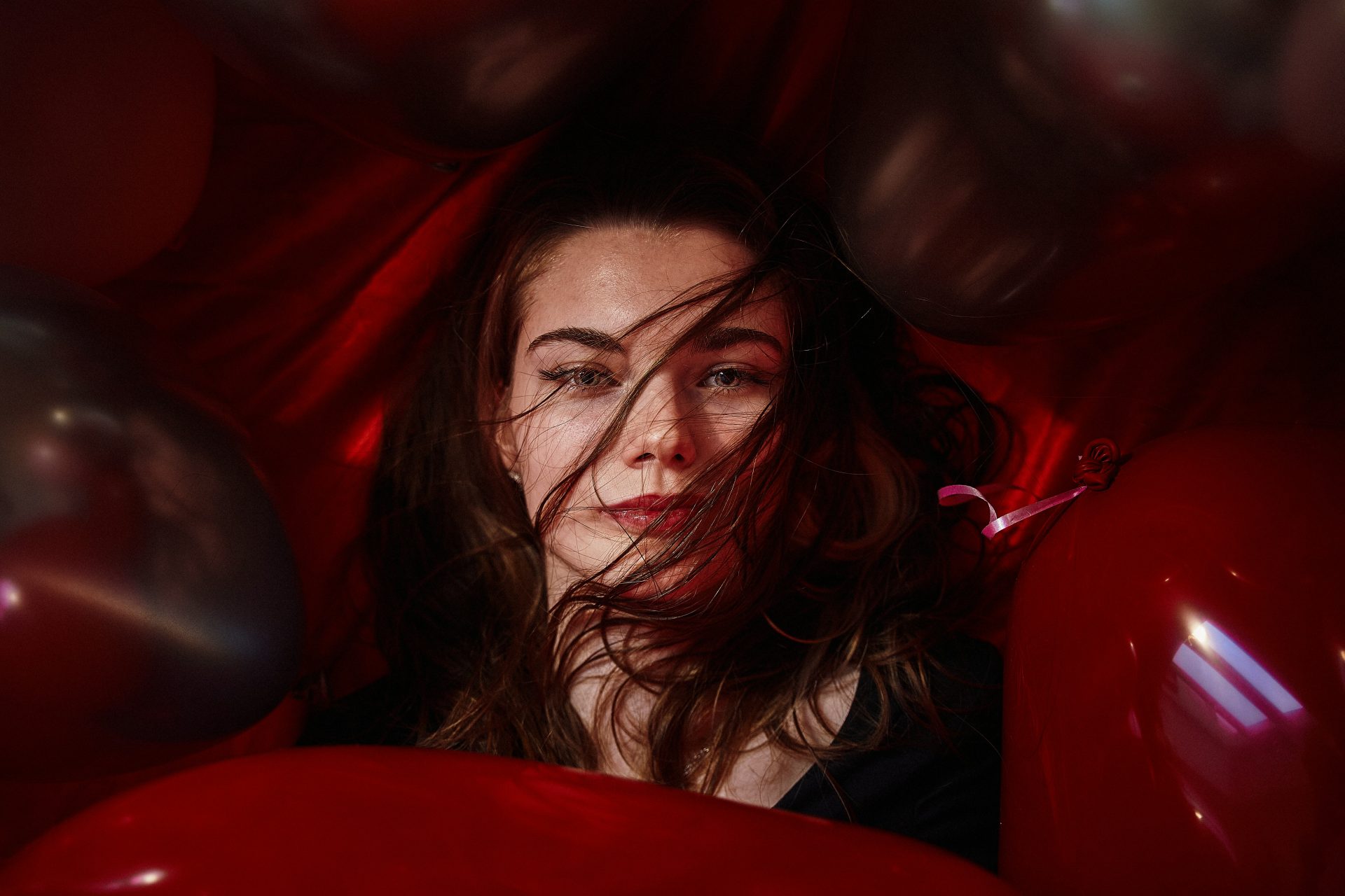 A woman is surrounded by red balloons